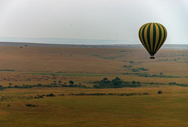 A striped hot-air balloon drifting over the Maasai Mara plains at dawn